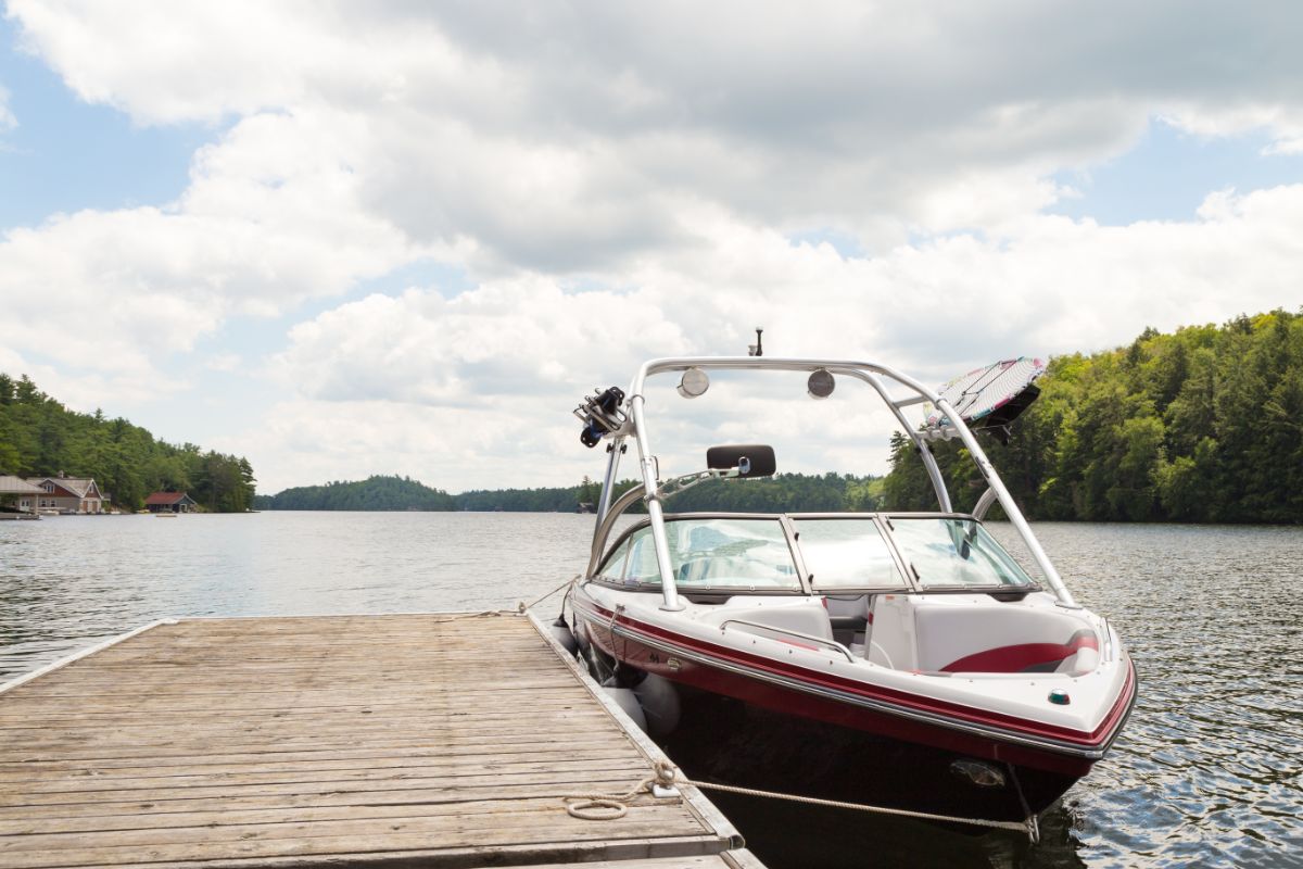 A wakeboard boat at a wooden dock on a sunny day.