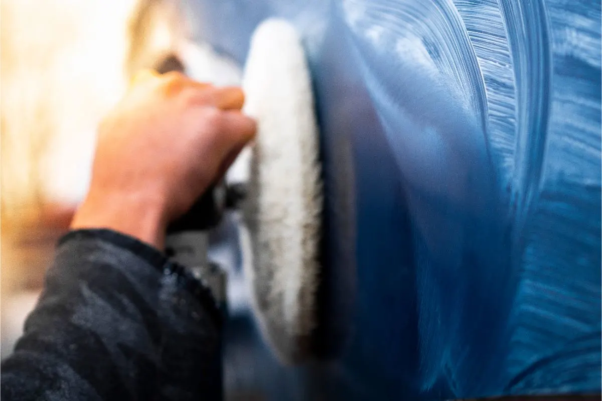 A mans hand compounding and waxing a boat hull.