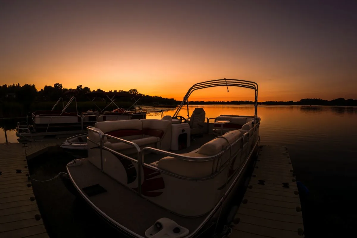 A landscape photo of lake sunset featuring docked pontoon boat.