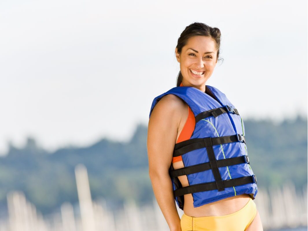 A woman smiling wearing life jacket on the beach.