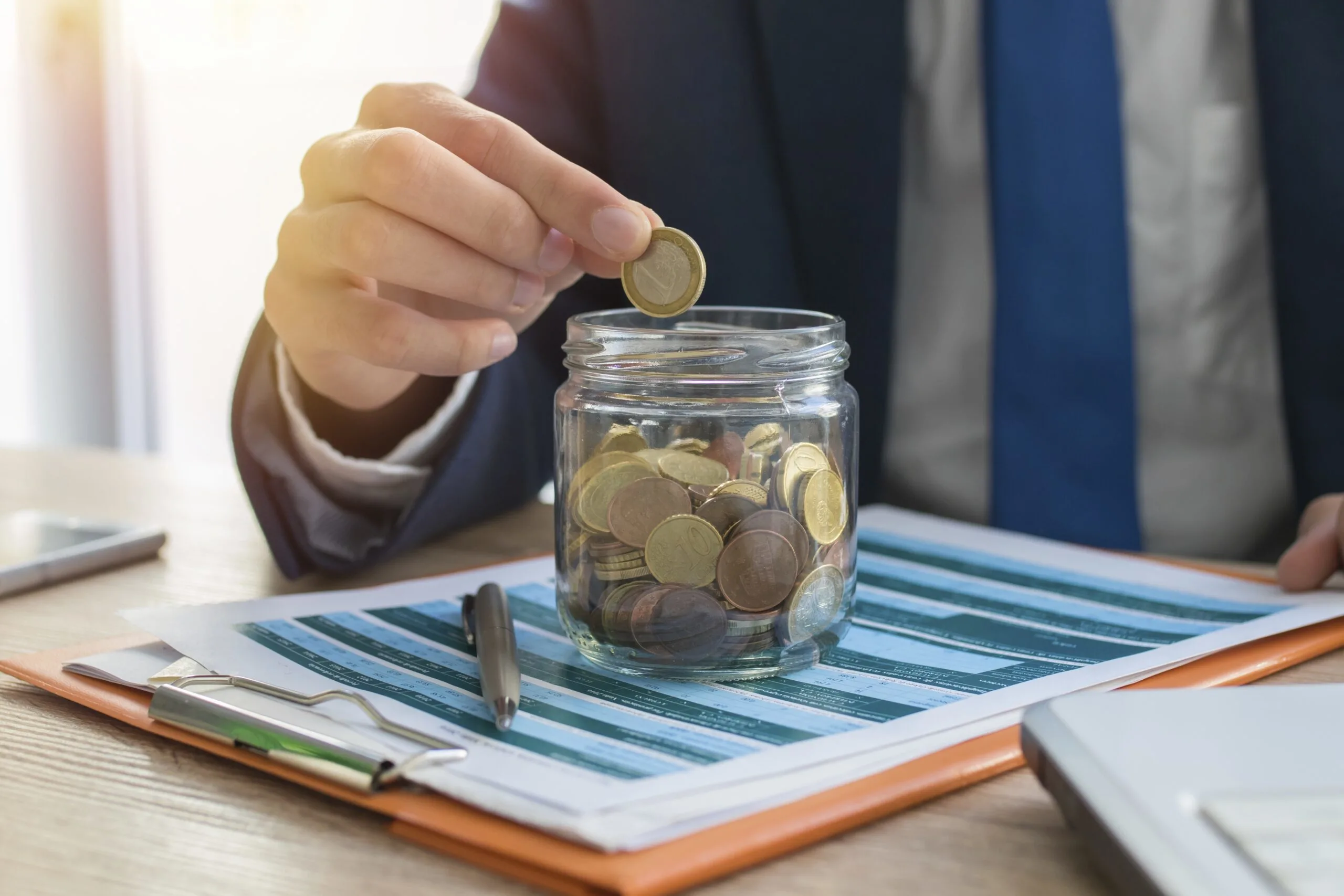 A business man saving coins in a jar.