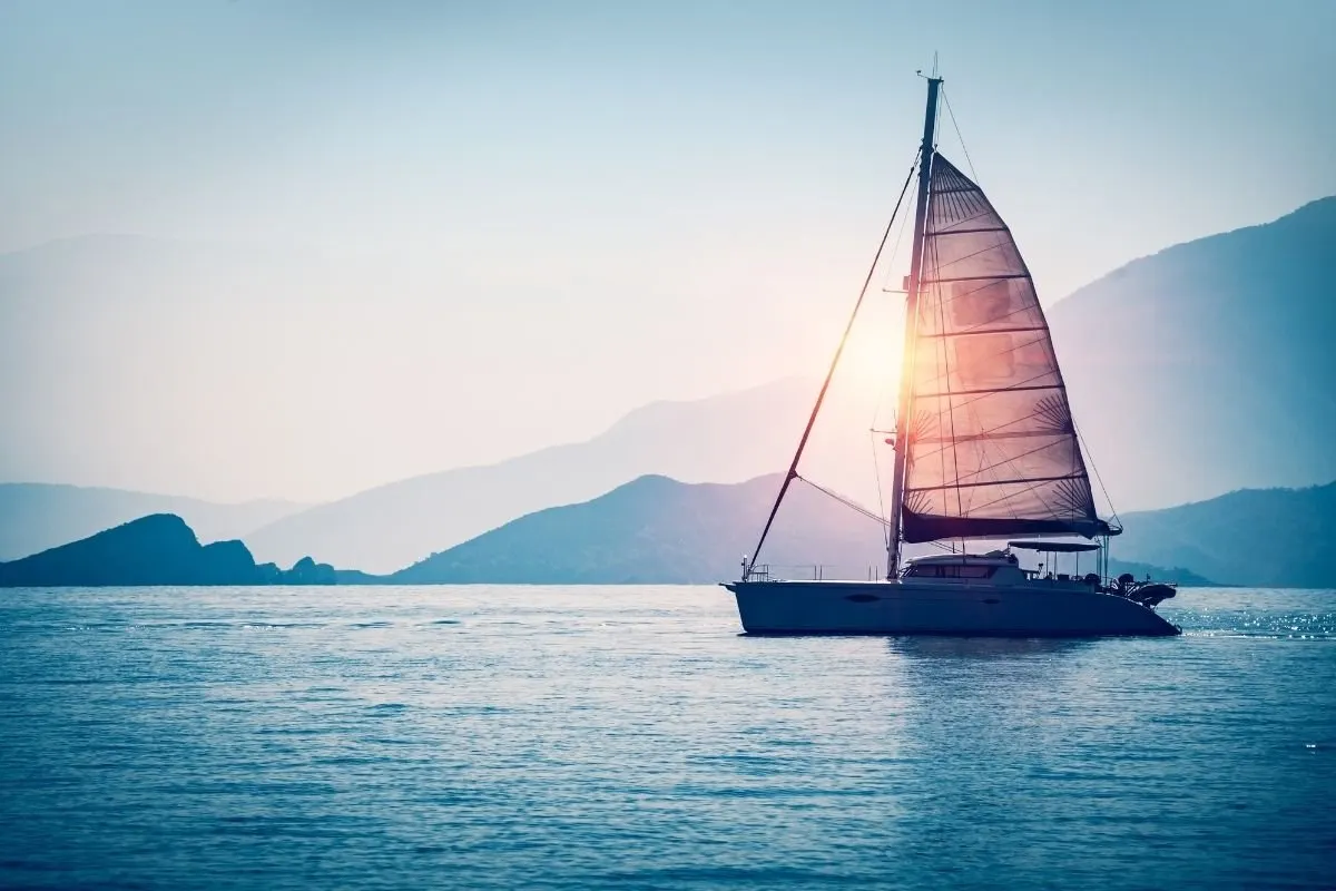 A photo of sailboat in the sea in the evening sunlight over beautiful big mountains background.