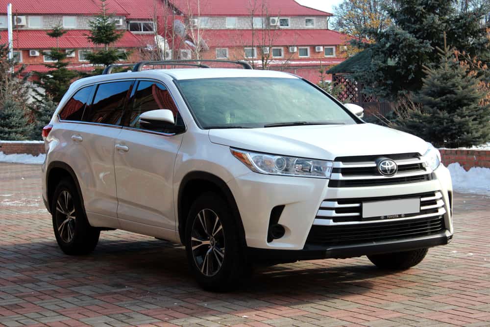 This is a close look at a white Toyota Highlander on a bricked driveway.