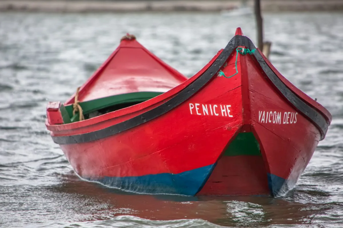 A small red boat with a Portugese name in a canal.