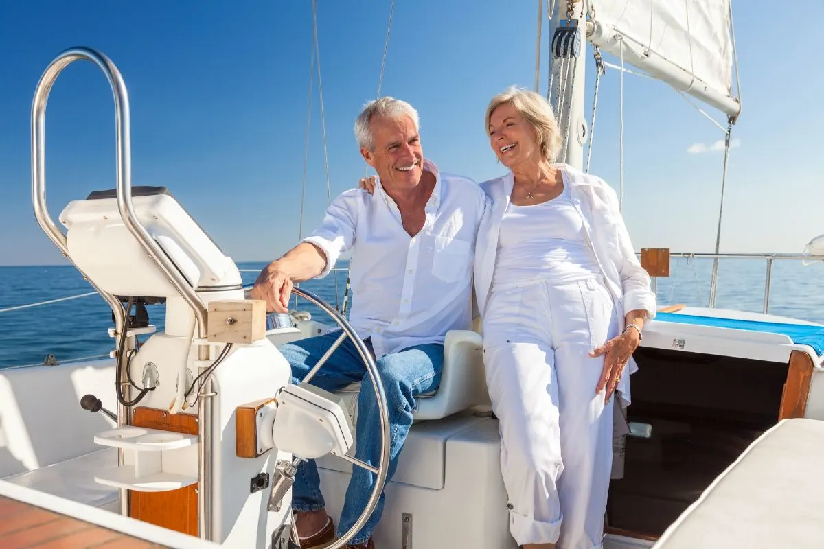 Cheerful couple both wearing white clothes are steering their motor boat on sea to enjoy during vacation.