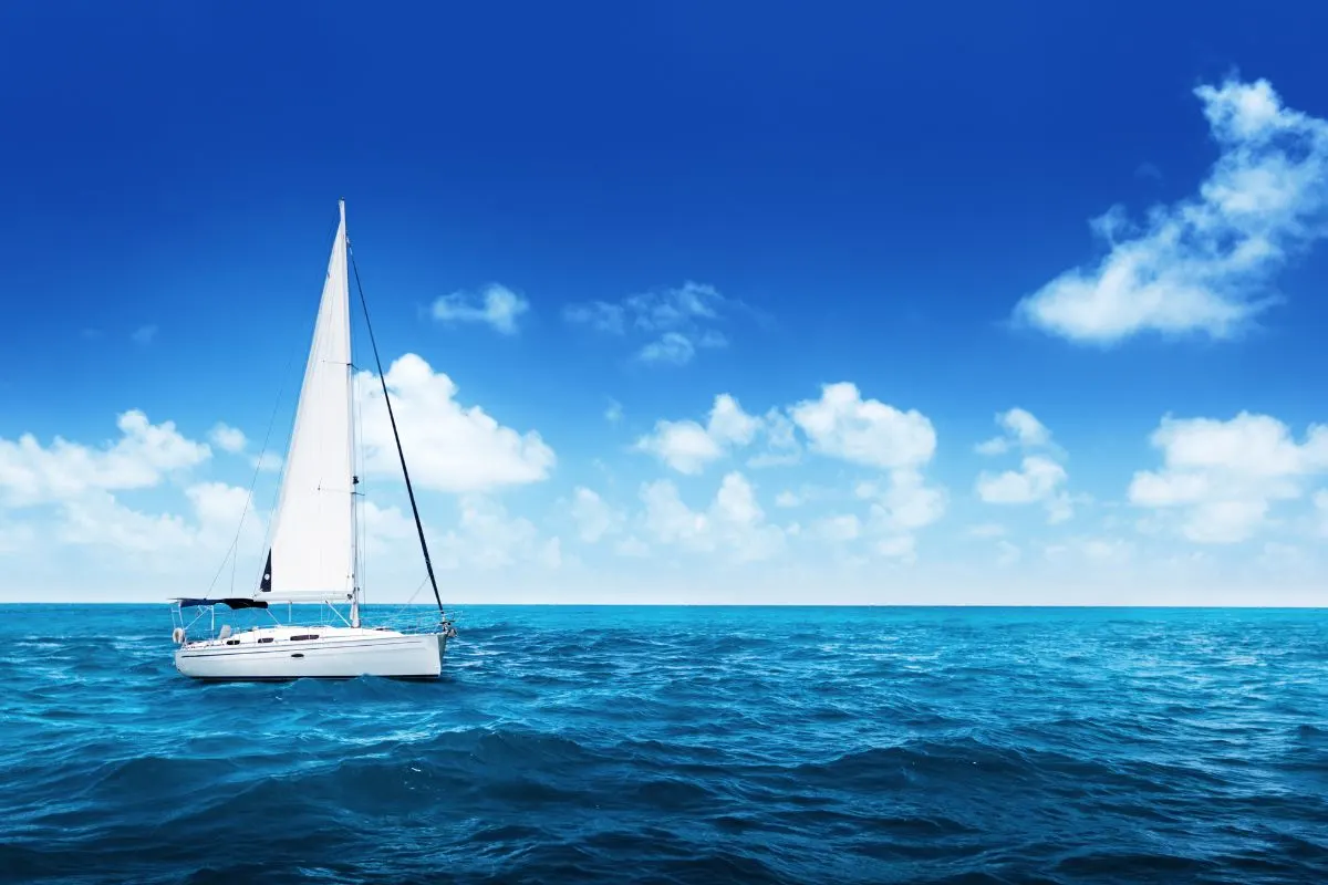 Side view photo of a white boat sailing on a blue ocean.