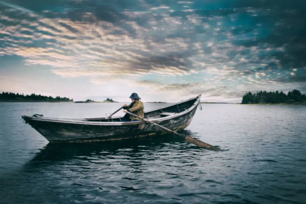 An adult man wearing a hat sailing to the sea with cloudy sky in the background.