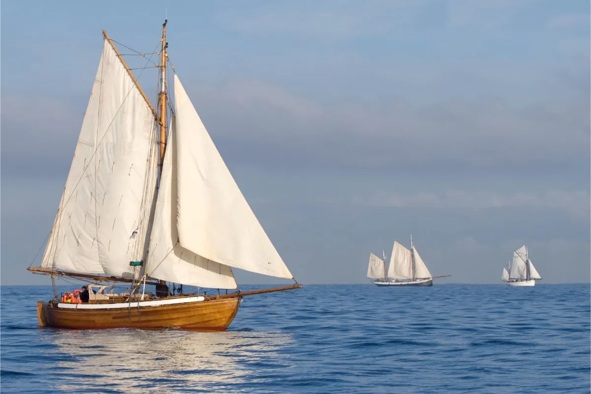 A photo of boat in a mizzen sails on the ocean with other boats.