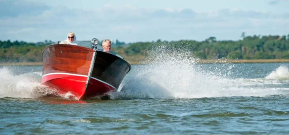 Two adult men speeding up a speed boat with a planing hull.