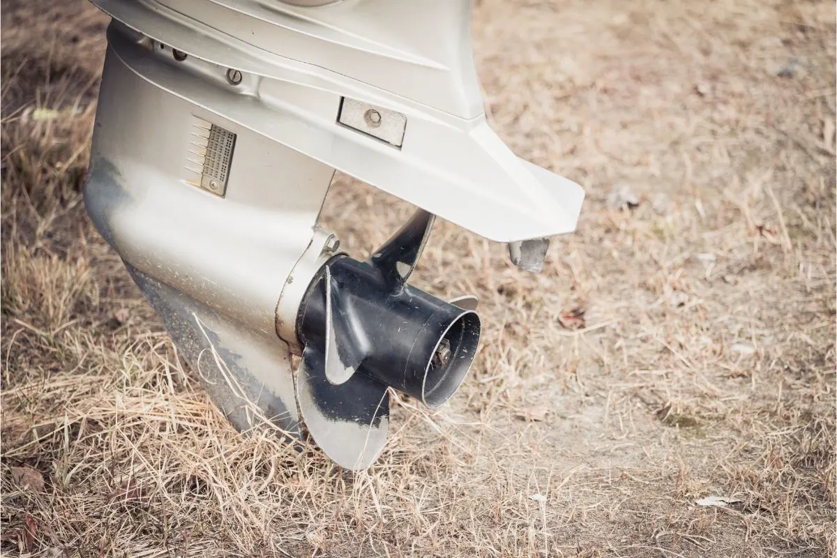 A large outboard motor with peeled propeller on the grassy shore.