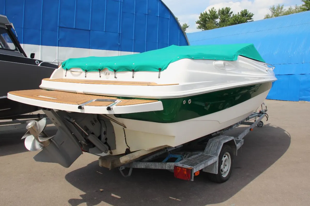 A white boat with a green strip and awning on the shore.