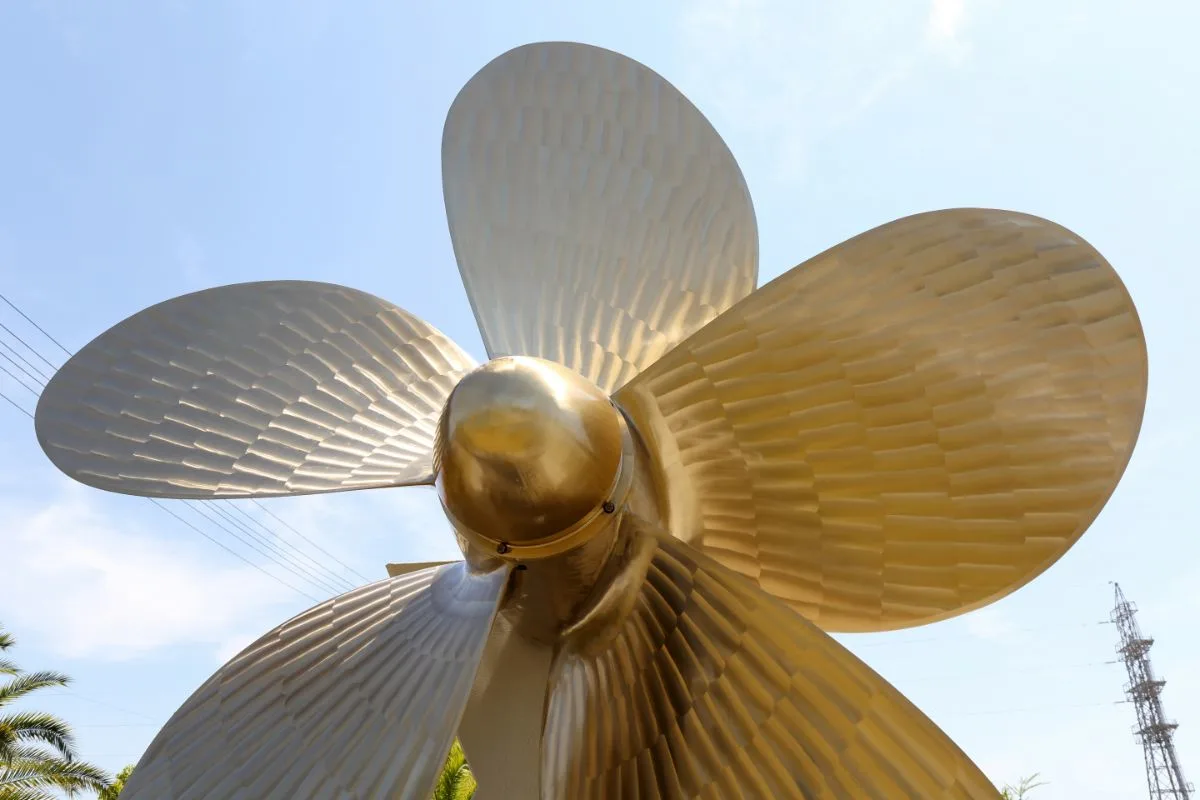 A five-bladed boat propeller in gold under the sky background.