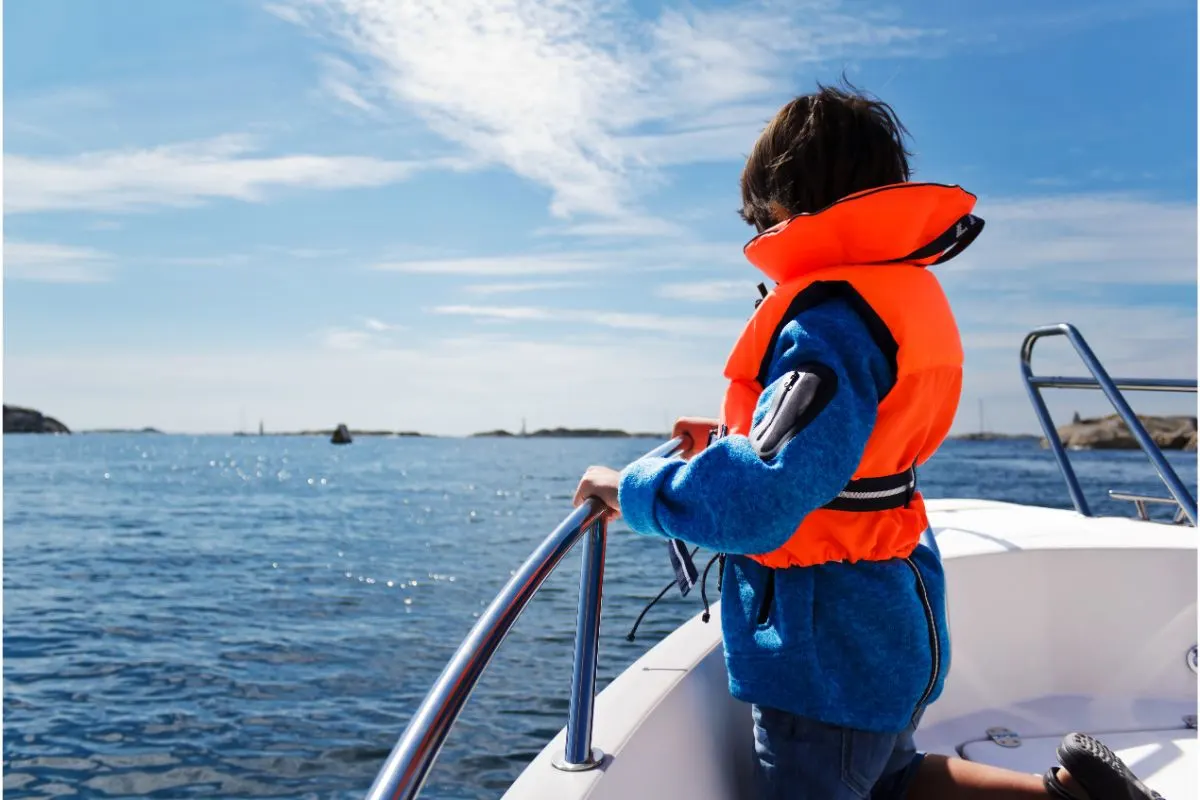 Back view of a kid wearing lifejacket for protection on yacht.