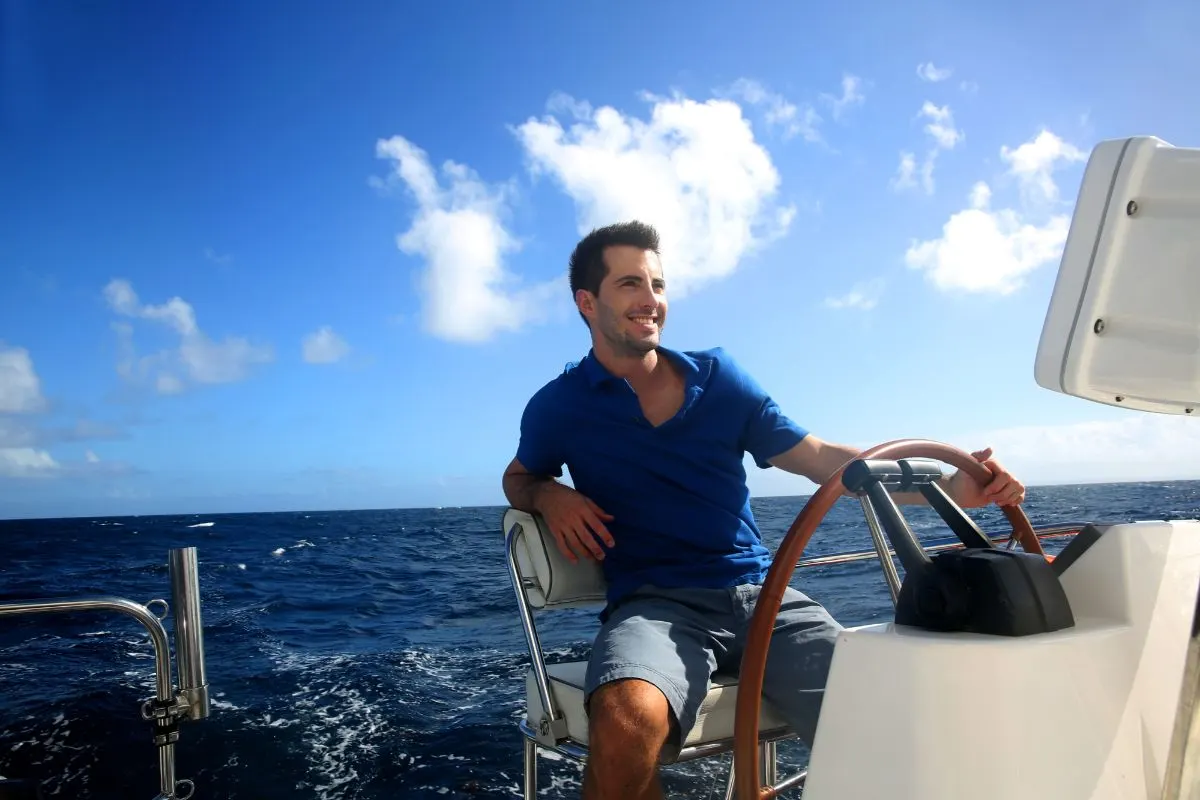 A smiling man driving his motor boat while holding unto his boat's steering wheel.