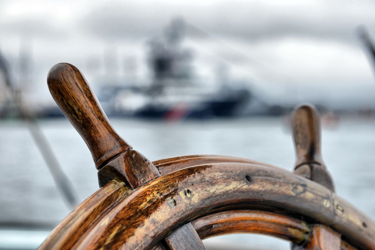 Zoom in half photo of a wooden steering wheel of a sailboat with blurred background.