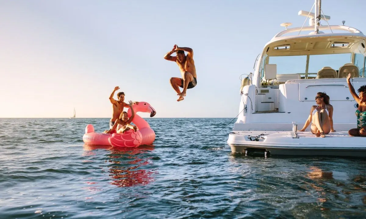 Group of friends enjoying a summer day with a man diving in the sea sitting on yacht and inflatable toy.