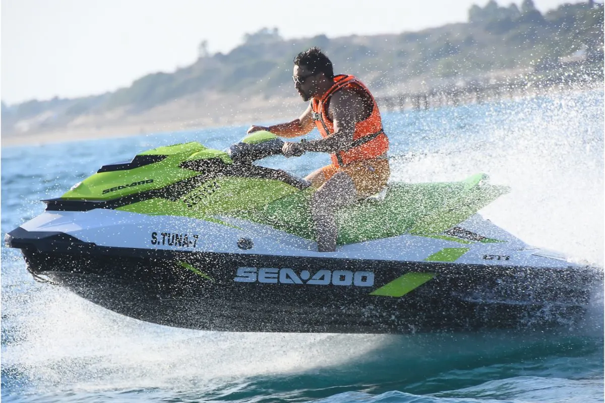 A man with orange vest driving a jetski in the sea.