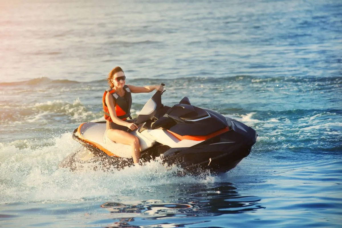 A sporty caucasian woman riding jet ski in ocean blue water at warm evening sunset.