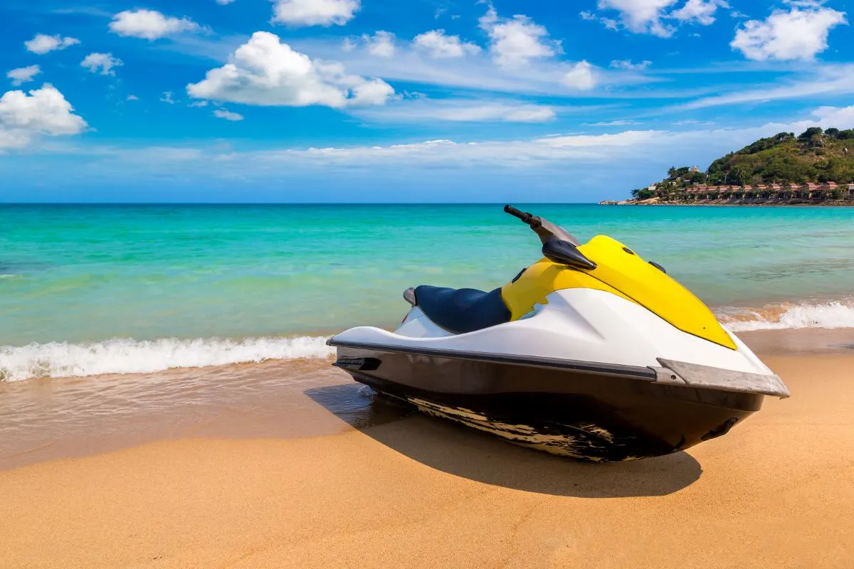 A combination of yellow and white colored jetski on the beach overlooking the hillside background.